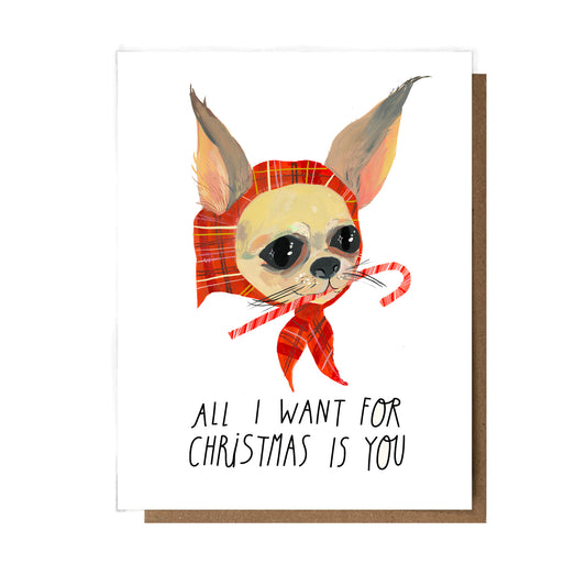 A white holiday greeting card with a Chihuahua wearing a red bonnet while eating a candy cane, text reading "All I Want For Christmas Is You."